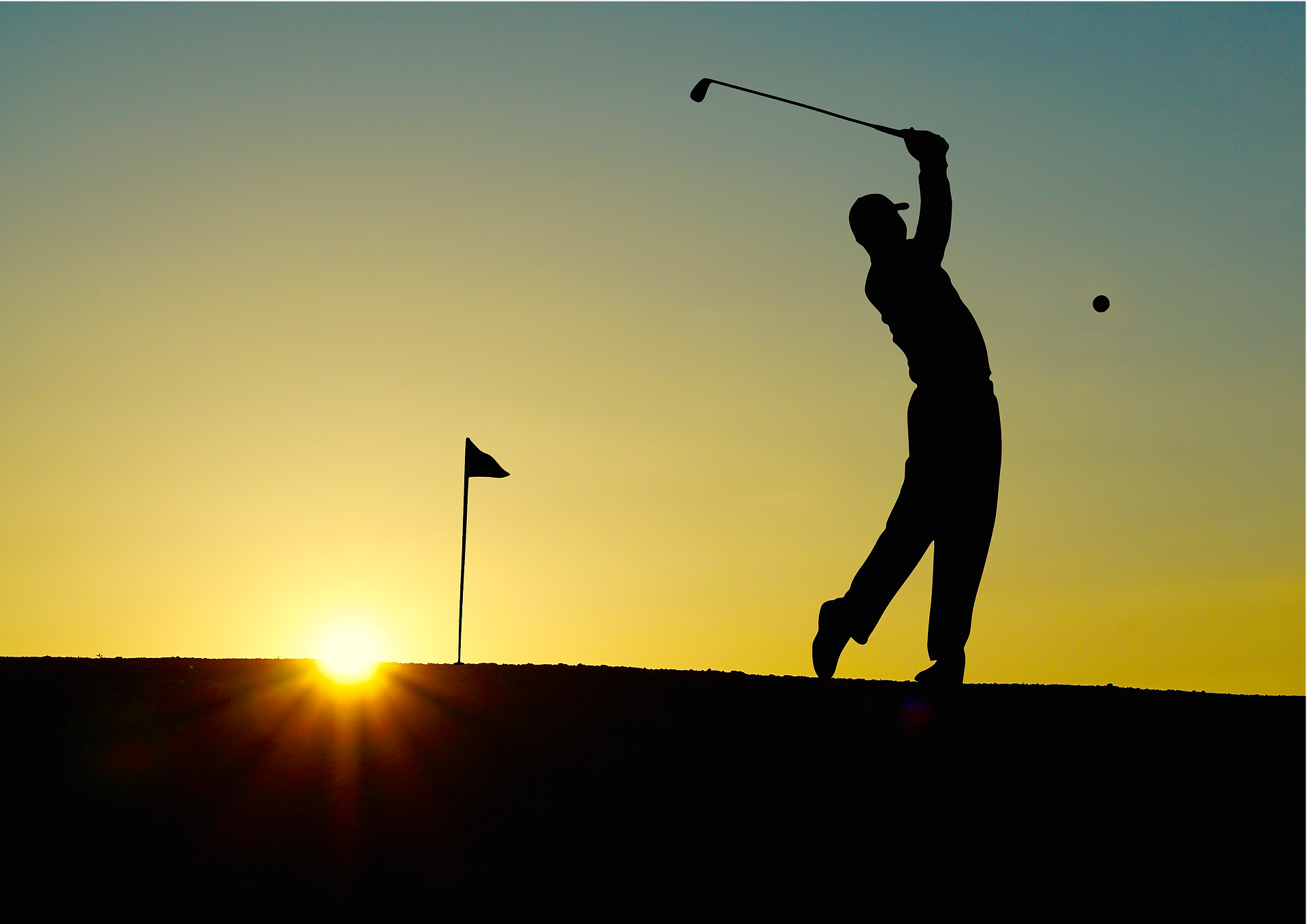 A golfer illuminated by the sunrise with the flag hole behind him