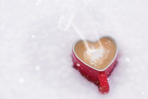 Cup of coffee in a heart-shaped mug sitting in snow