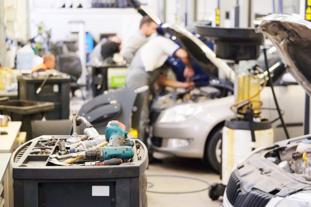 A tool trolley in the foreground of a busy auto repair shop with mechanics working in the background.
